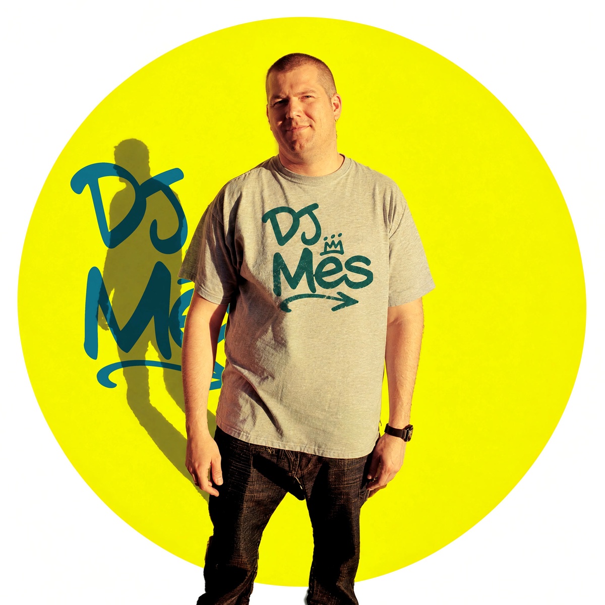 DJ Mes standing in front of a yellow circle covered in the djmes logo